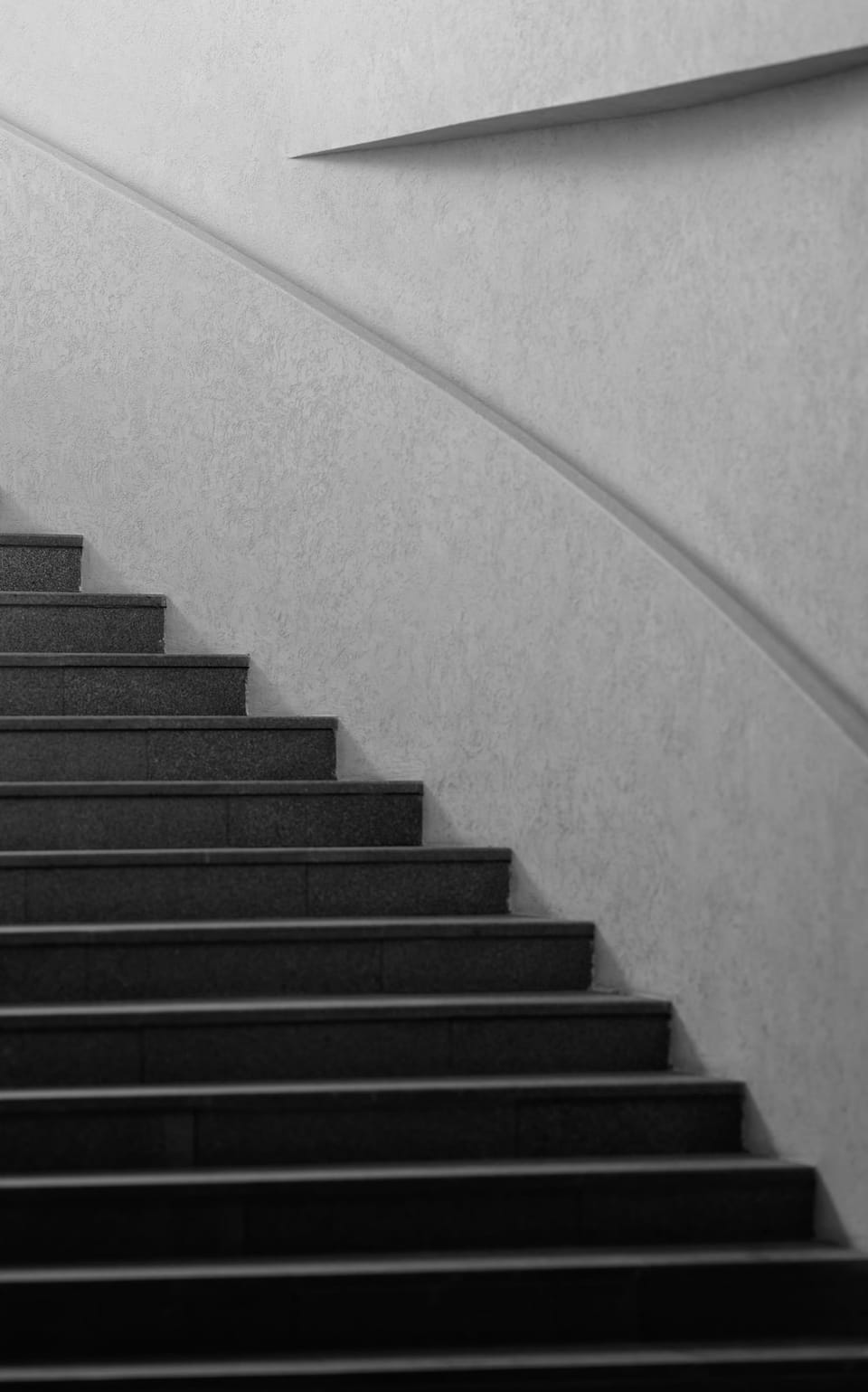 Precast concrete staircase curving up beside a plastered wall